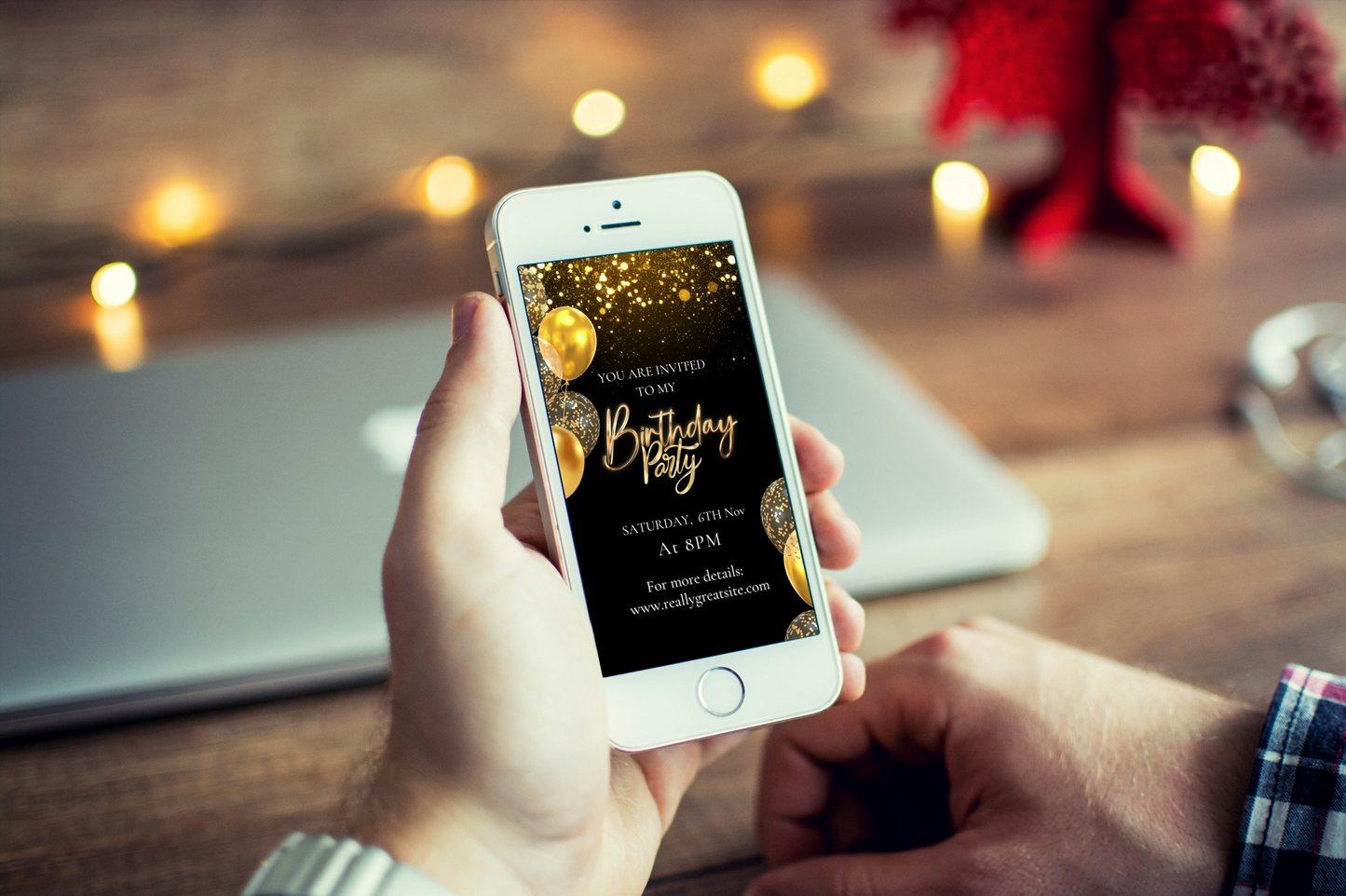 Hand holding a smartphone with a birthday party invitation on a blurred background of a cozy room.