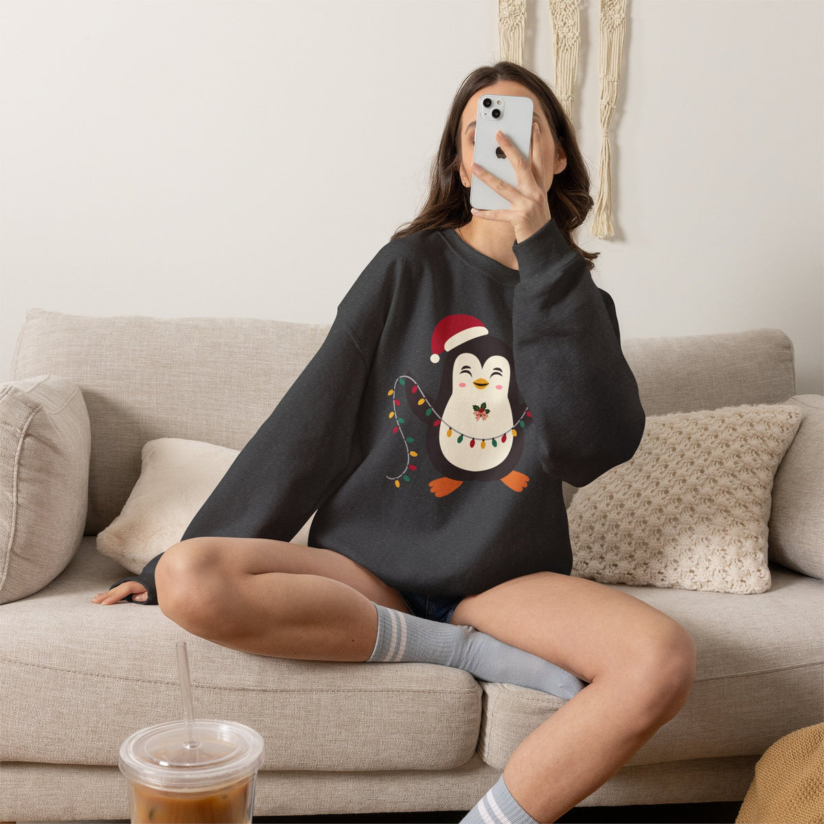 Person sitting on a couch wearing a black sweatshirt with a symbol, holding a phone.