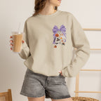 A woman wearing a beige crewneck sweatshirt with a purple and orange Halloween-themed graphic on the chest, paired with gray denim shorts and holding an iced coffee.