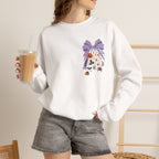 A woman wearing a white crewneck sweatshirt with a purple and orange Halloween-themed graphic print, paired with gray denim shorts and holding an iced coffee.
