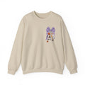 A beige crewneck sweatshirt featuring a whimsical embroidered design on the left chest of a purple patterned bow, a white cat, and small orange flowers, displayed against a clean white background.