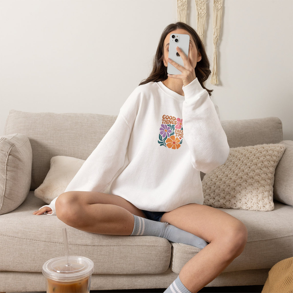 Person wearing a white sweatshirt with a logo, sitting on a couch in a living room.