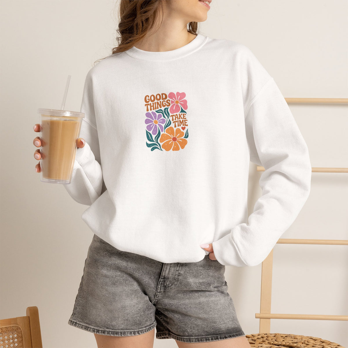 A woman wearing a white crewneck sweatshirt with a black graphic that reads 'BRIDE to Be' above an illustration of a bride in a margarita glass, paired with gray denim shorts and holding an iced coffee.